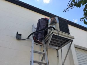Coolco employee on a ladder servicing an elevated AC unit